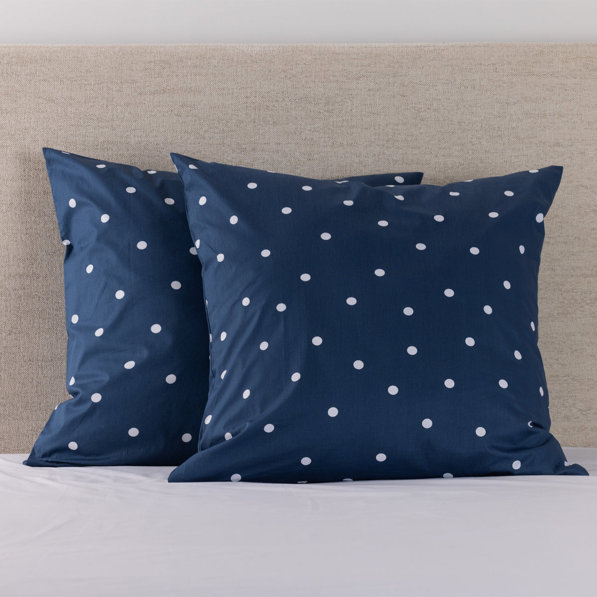 Pure & Simple Monroe European Pillowcase Pair in white with olive polka dots, styled on a bed against a neutral upholstered headboard.