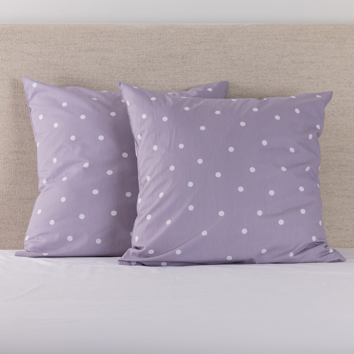 Pure & Simple Monroe European Pillowcases in lilac, featuring a white polka dot design, displayed on a bed with a neutral upholstered headboard.