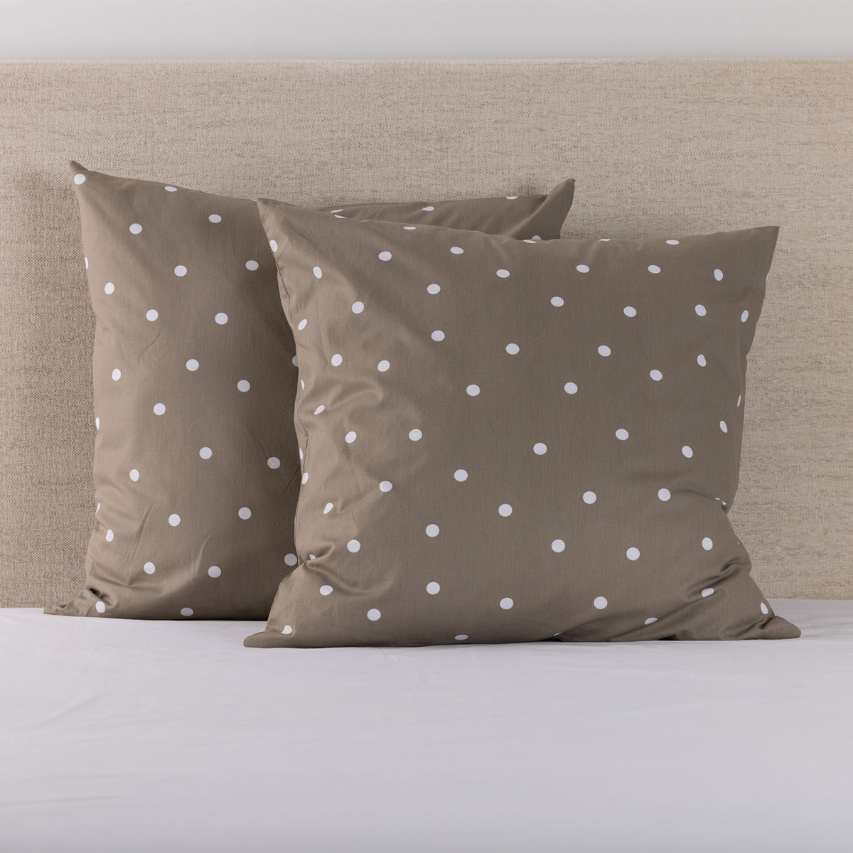 Pure & Simple Monroe European Pillowcases in mocha, featuring a white polka dot design, styled on a bed against a neutral upholstered headboard.