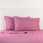 Berry linen pillowcases are beautifully layered against a white panelled headboard, showcasing their natural woven texture and relaxed, contemporary elegance.