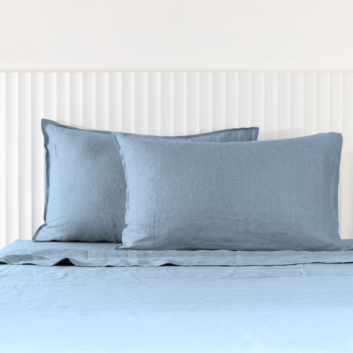 Denim linen pillowcases are beautifully layered against a white panelled headboard, showcasing their natural woven texture and relaxed, contemporary elegance.