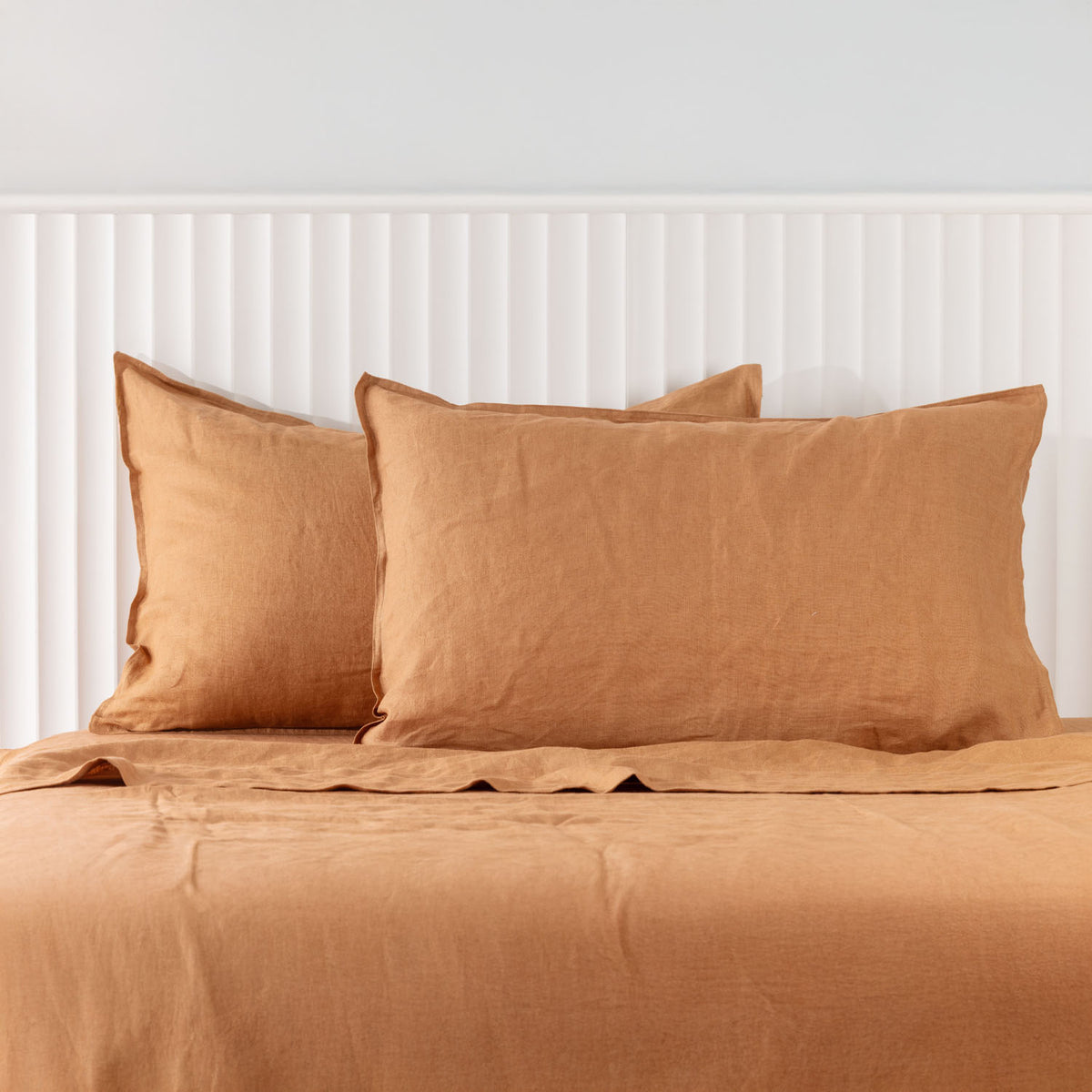 Pecan linen pillowcases are beautifully layered against a white panelled headboard, showcasing their natural woven texture and relaxed, contemporary elegance.