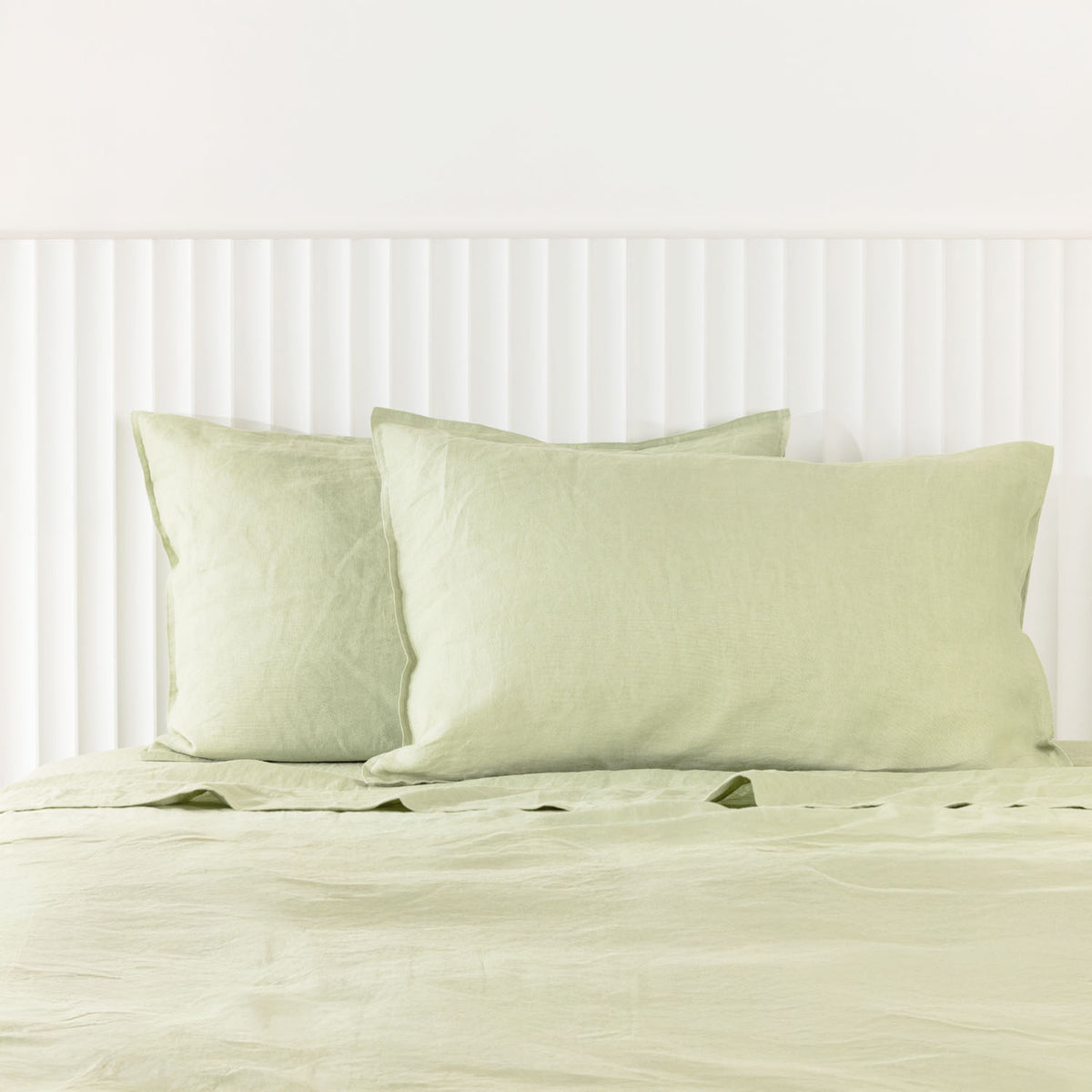Pistachio linen pillowcases are beautifully layered against a white panelled headboard, showcasing their natural woven texture and relaxed, contemporary elegance.