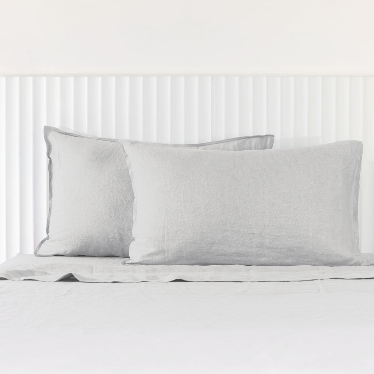 Silver linen pillowcases are beautifully layered against a white panelled headboard, showcasing their natural woven texture and relaxed, contemporary elegance.