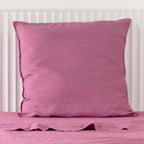 A berry linen Euro pillowcase is elegantly styled against a white panelled headboard, showcasing its generous square shape, soft natural texture and relaxed, timeless appeal.