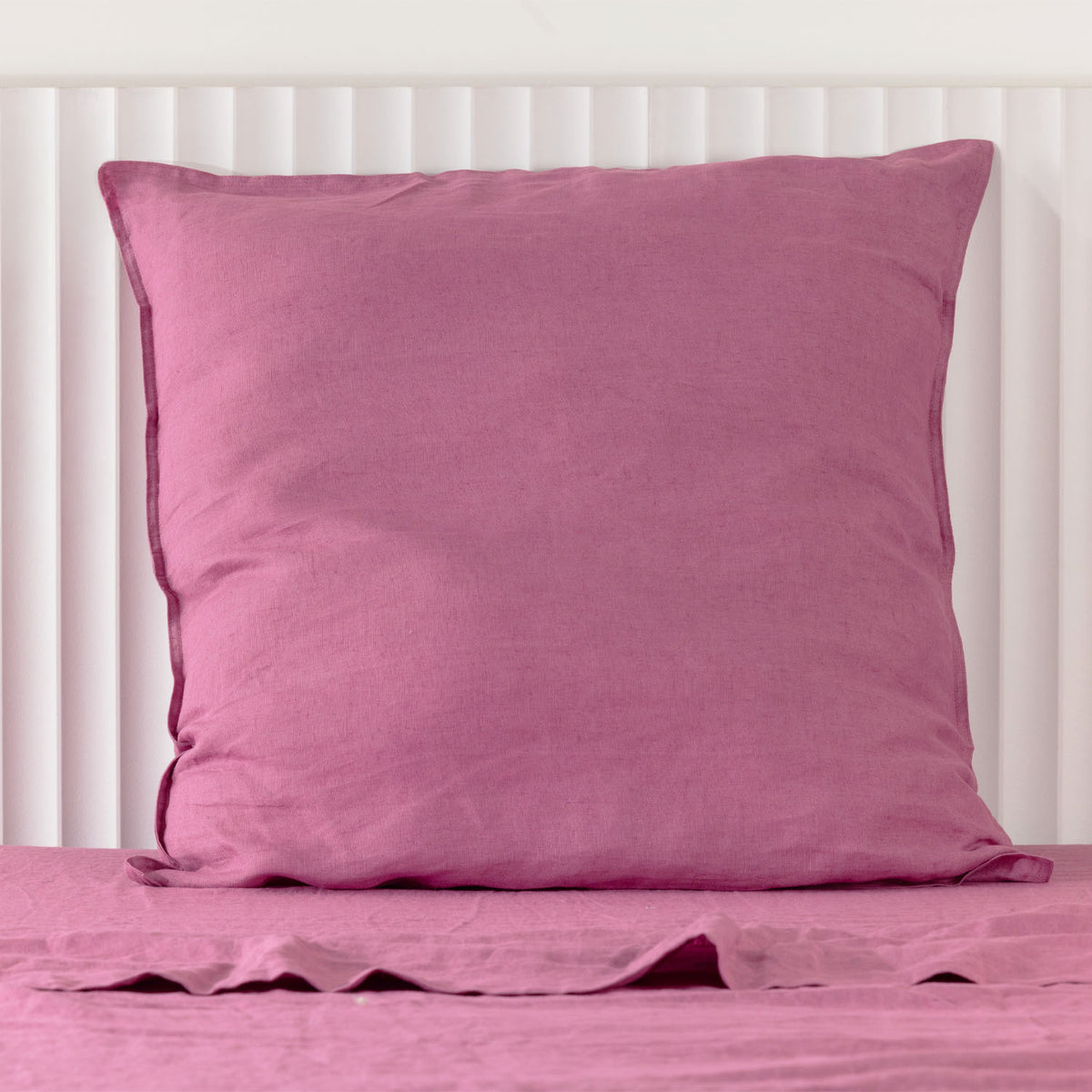 A berry linen Euro pillowcase is elegantly styled against a white panelled headboard, showcasing its generous square shape, soft natural texture and relaxed, timeless appeal.
