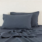 Midnight linen pillowcases are beautifully layered against a neutral textured backdrop, showcasing their natural, relaxed texture and timeless elegance.