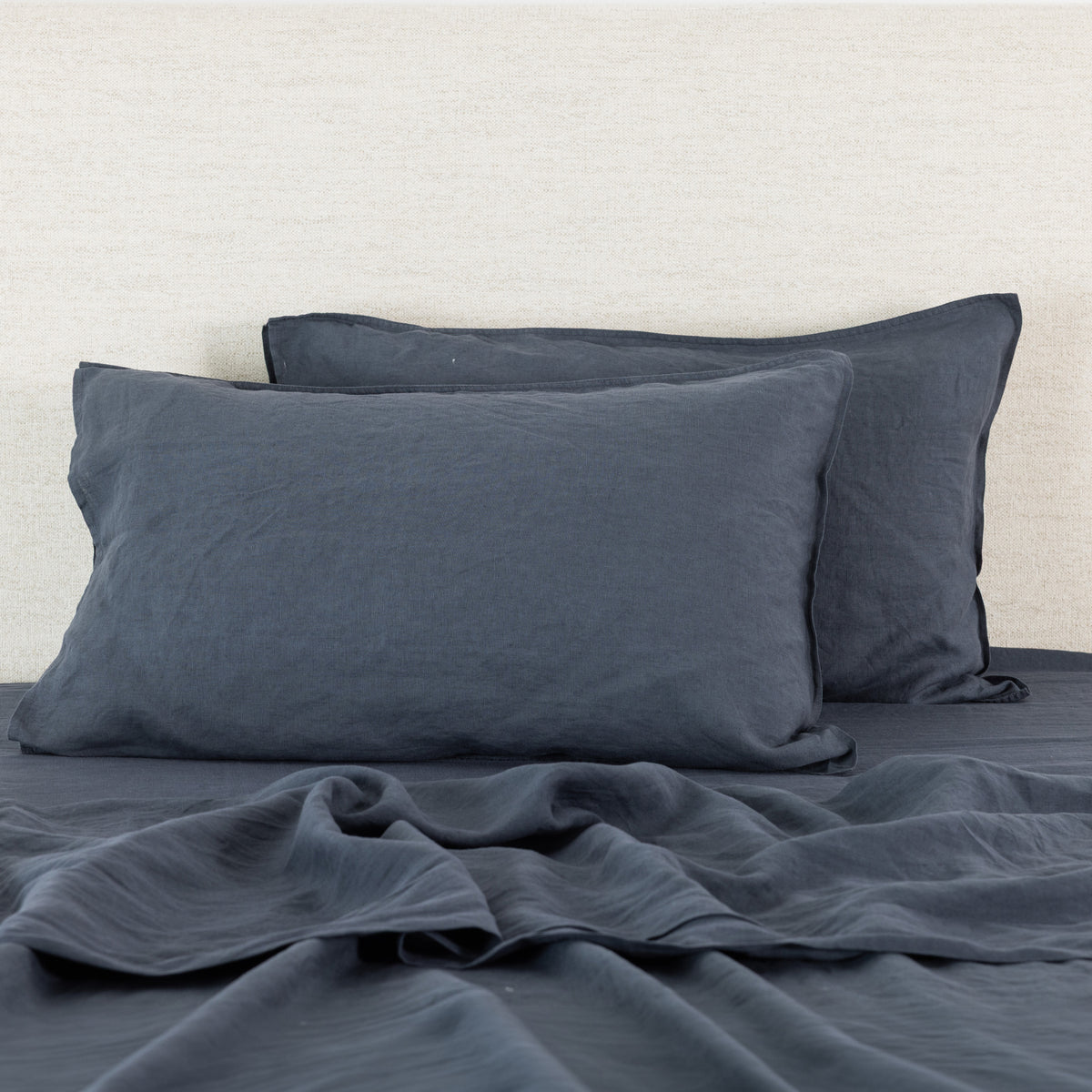 Midnight linen pillowcases are beautifully layered against a neutral textured backdrop, showcasing their natural, relaxed texture and timeless elegance.