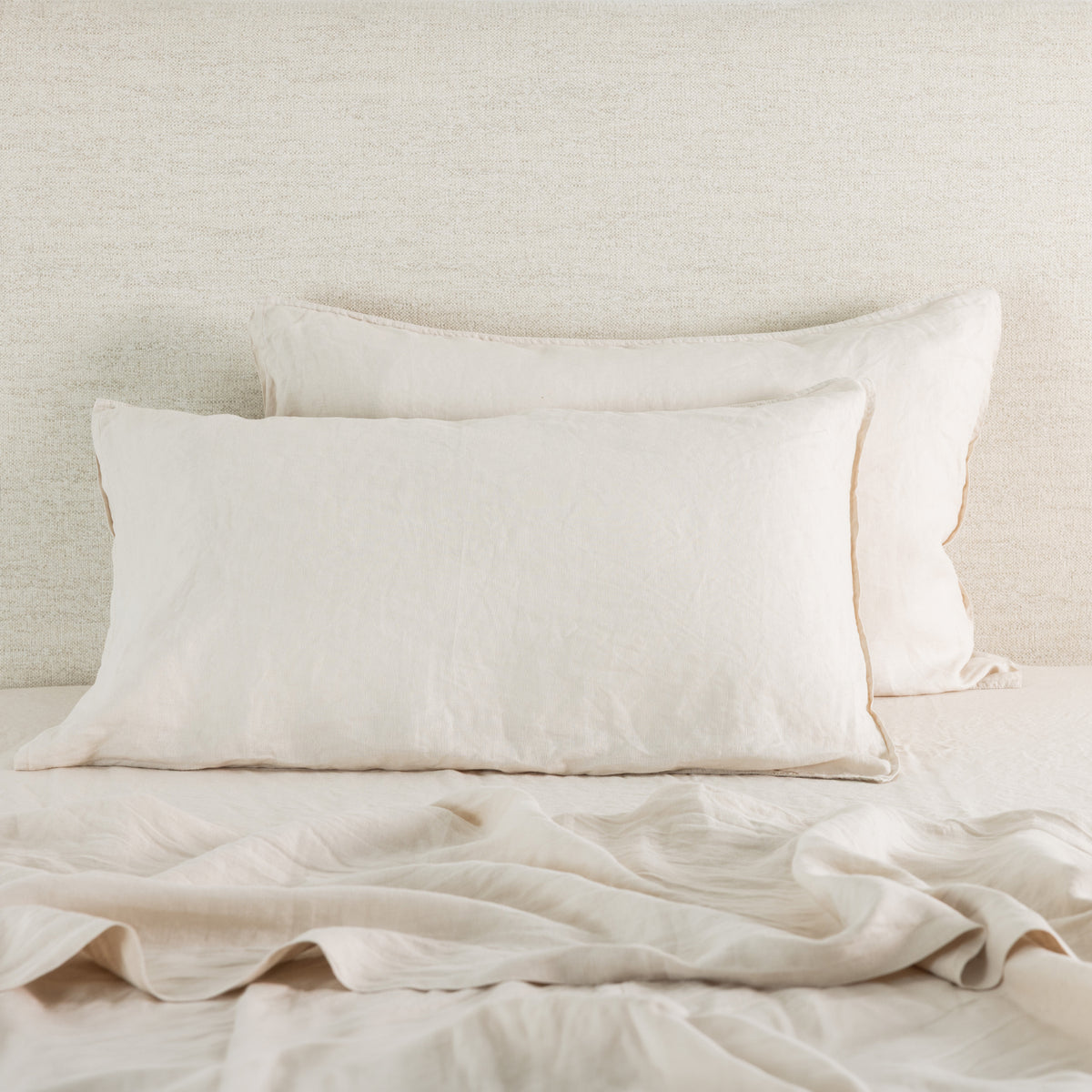 Soft natural linen pillowcases are beautifully layered against a neutral textured backdrop, showcasing their natural, relaxed texture and timeless elegance.