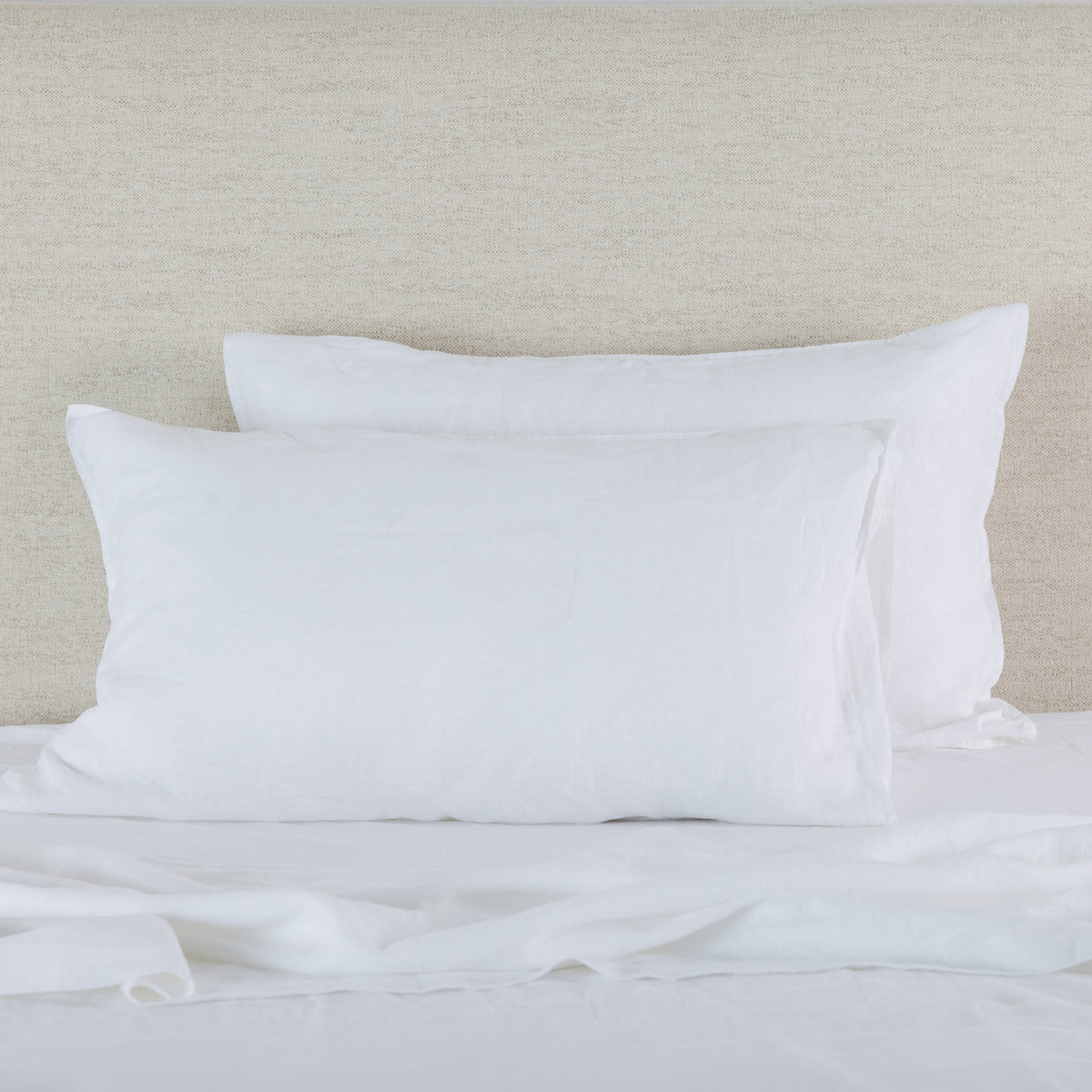 Soft white linen pillowcases are beautifully layered against a neutral textured backdrop, showcasing their natural, relaxed texture and timeless elegance.