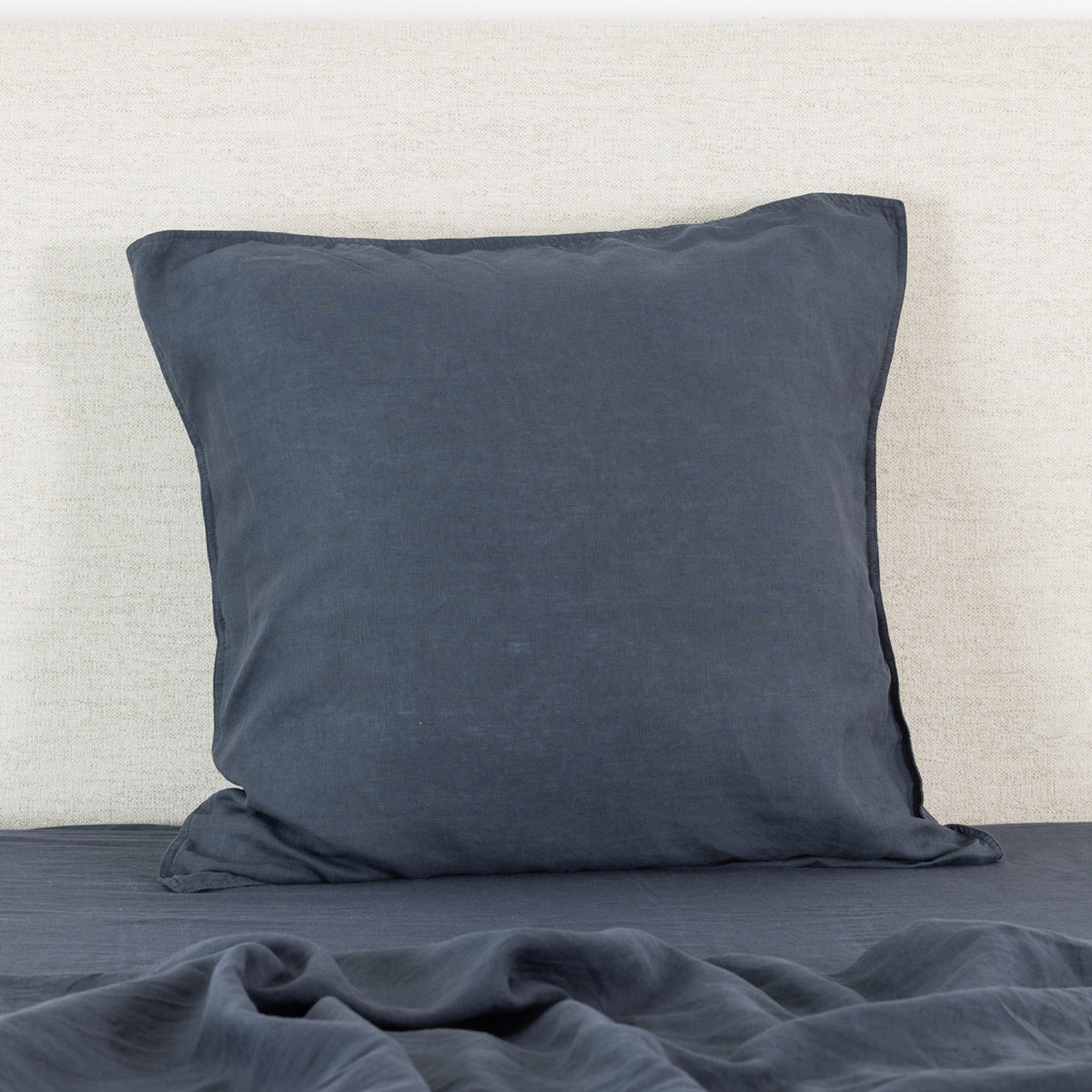 A midnight linen Euro pillowcase is elegantly styled against a neutral textured backdrop, highlighting its generous square shape, natural linen texture and relaxed, timeless appeal.