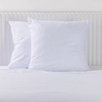 Two white Euro pillowcases with fine blue horizontal stripes styled on a white bed.