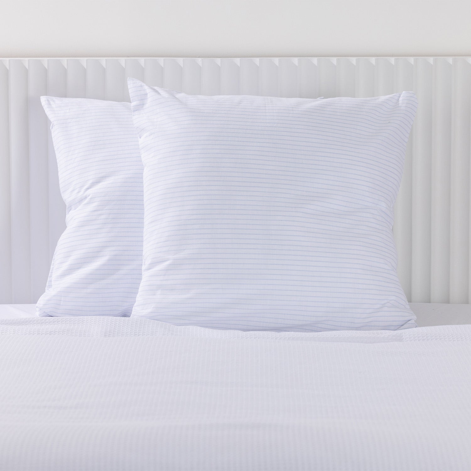 Two white Euro pillowcases with fine blue horizontal stripes styled on a white bed.