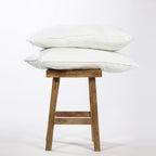 Two white pillows stacked on a wooden stool against a white background