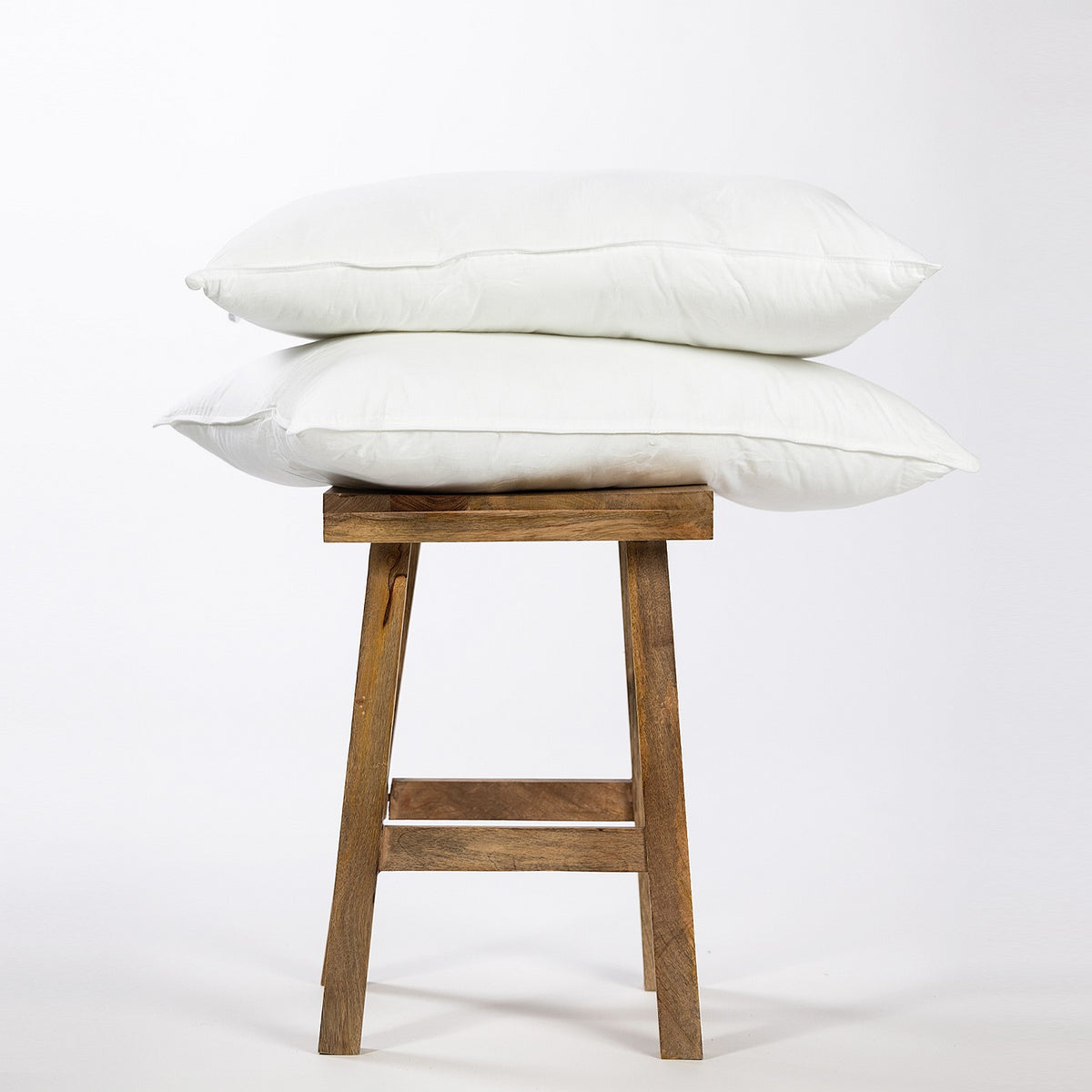 Two white pillows stacked on a wooden stool against a white background