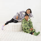 Two children wearing cosy hooded towels, one in green dinosaur print and one in purple unicorns print.