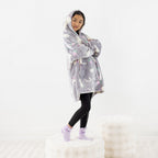 Child wearing a purple unicorn print hooded towel while standing on a white rug.