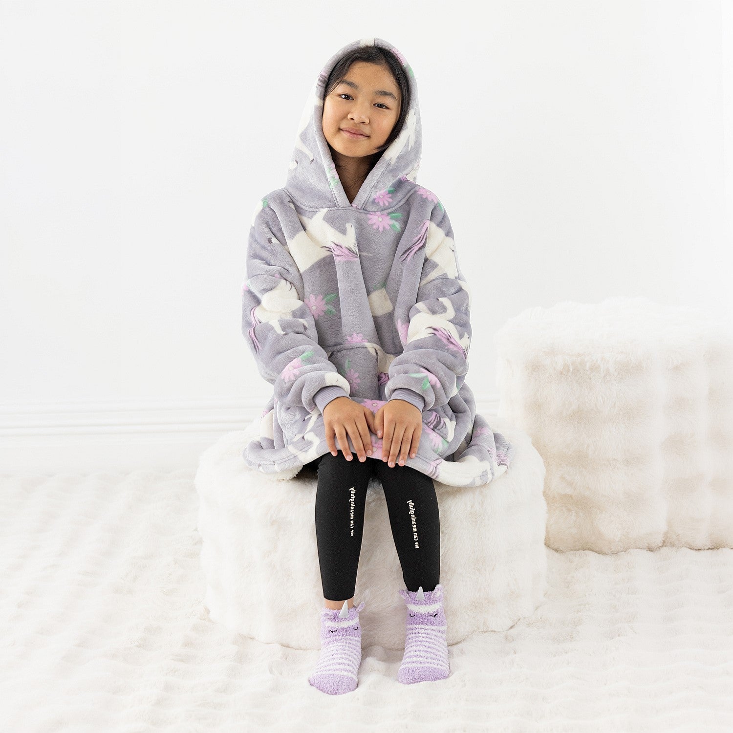 Child wearing a purple unicorn print hooded towel while standing on a white rug.