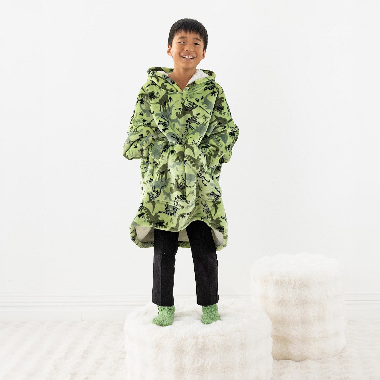 Child wearing a green dinosaur print hoodie while standing on a white stool.