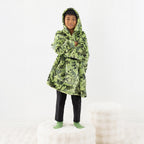 Child wearing a green dinosaur print hoodie while standing on a white stool.