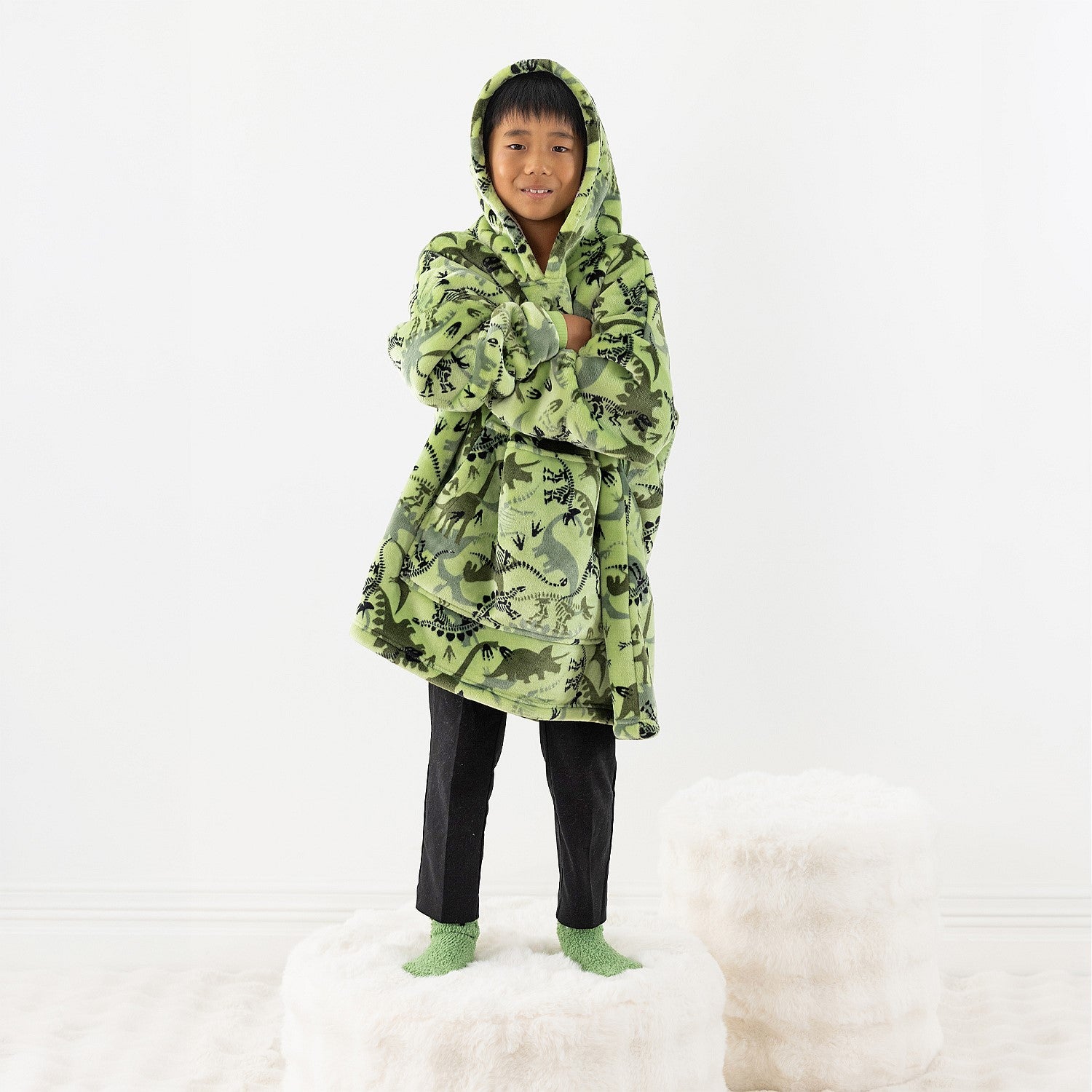 Child wearing a green dinosaur print hoodie while standing on a white stool.