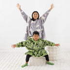 Two children wearing cosy hooded towels, one in green dinosaur print and one in purple unicorns print.