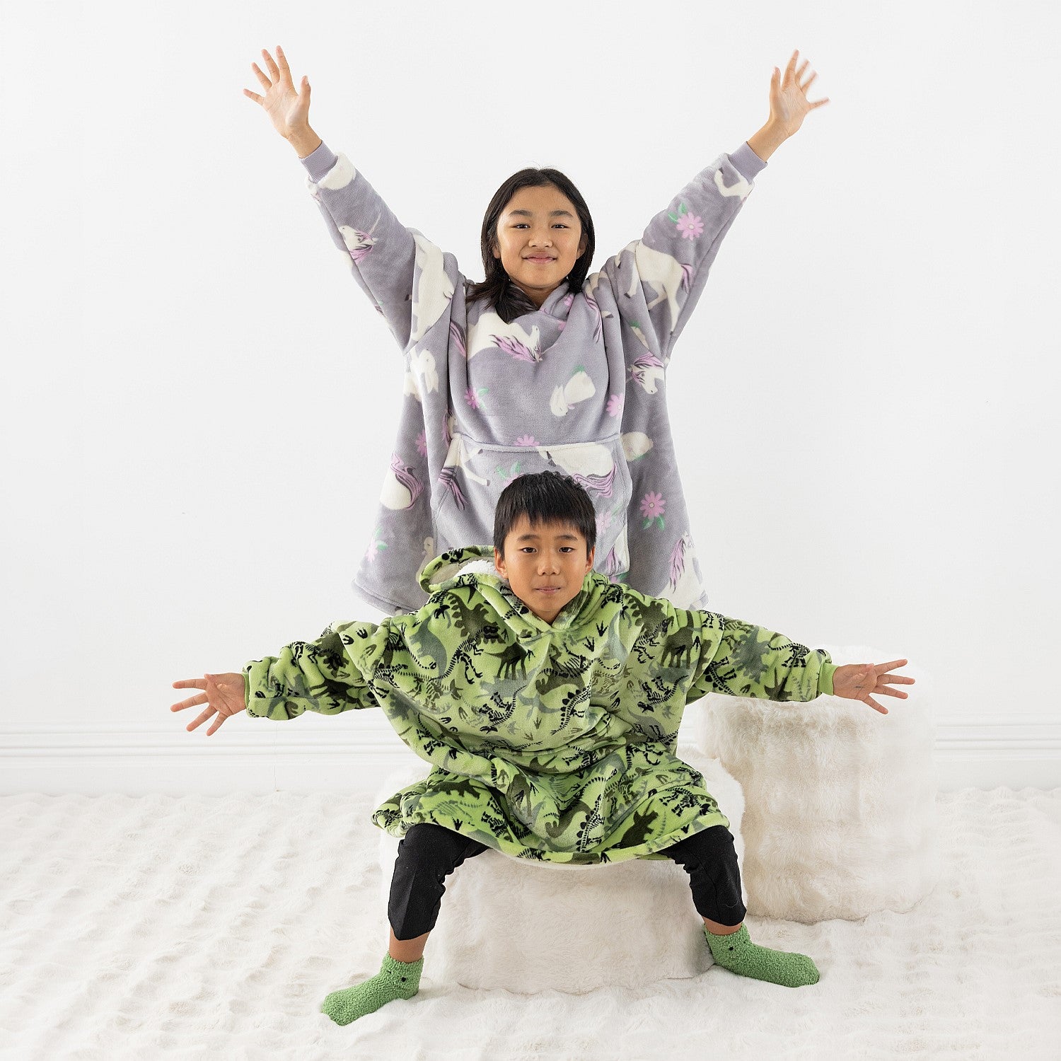 Two children wearing cosy hooded towels, one in green dinosaur print and one in purple unicorns print.