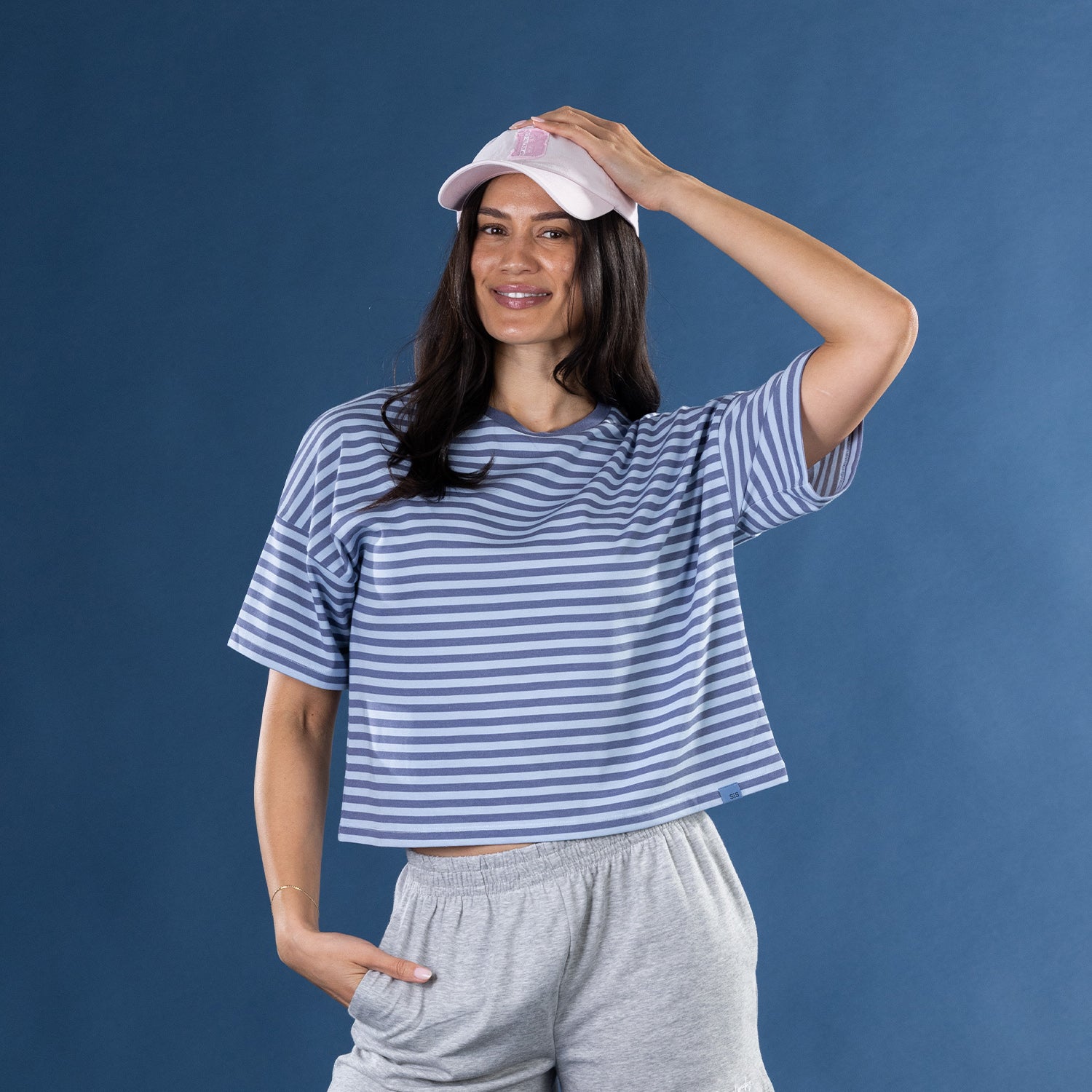 Woman wearing the Simple & Sunday Lounge Relaxed Stripe Tee in Faded Blue with grey lounge shorts and a pink cap.
