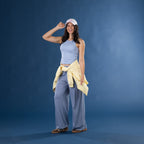 Model wearing the Faded Blue Simple & Sunday Lounge Weekend Ribbed Tank Top with striped lounge pants, a yellow sweatshirt tied around the waist, a white cap and slippers.