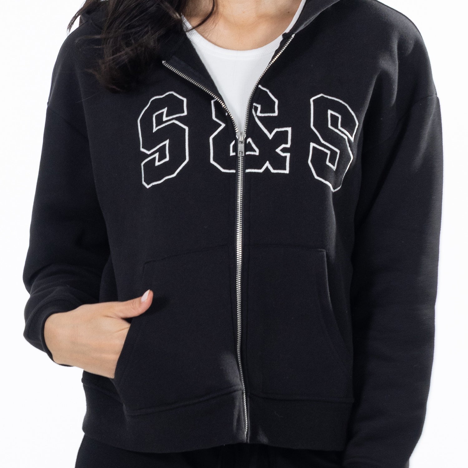 A person wearing a black zip-up hoodie with large white outlined 'S&S' lettering across the chest, layered over a white crew-neck T-shirt, against a plain white background.