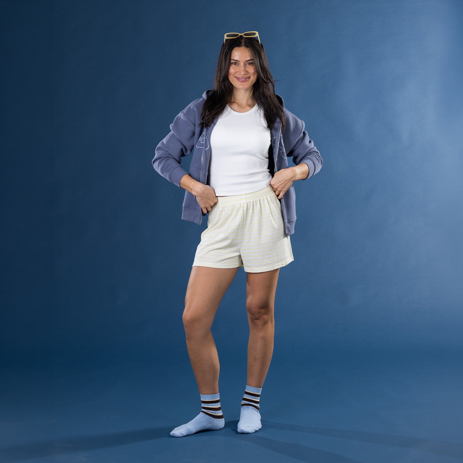 Model wearing yellow striped lounge shorts with a white ribbed tank top and blue zip hoodie.