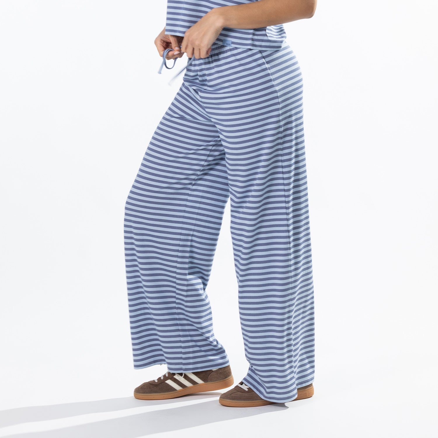 Close-up of the model wearing faded blue striped lounge pants, highlighting the drawstring waistband and wide-leg fit.