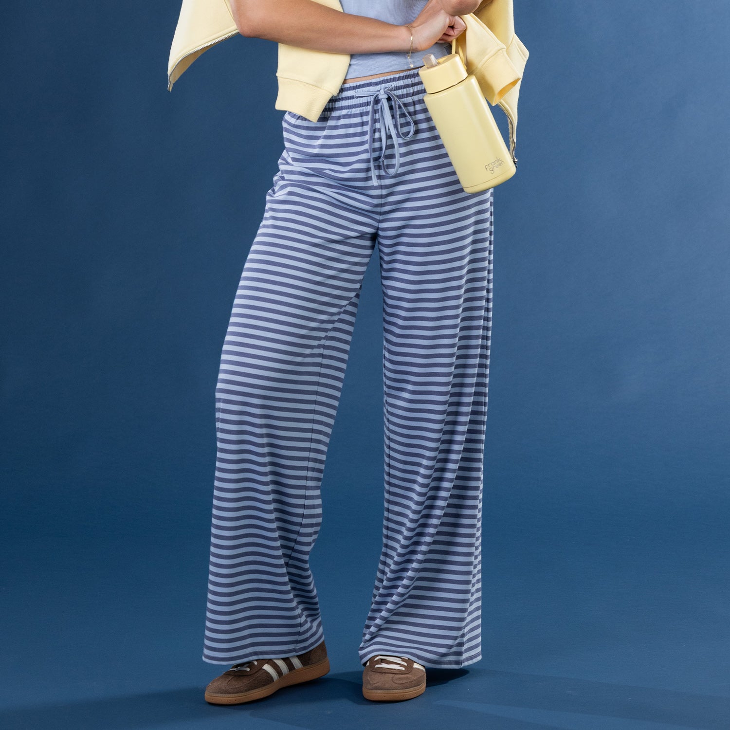 Close-up of the model wearing faded blue striped lounge pants with a blue ribbed tank top and yellow zip hoodie.