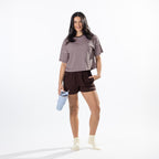 A woman modeling a brown and white striped short-sleeve t-shirt and dark brown athletic shorts, holding a light blue water bottle against a clean white studio background.