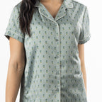 Close-up of the sage pyjama top, highlighting the button front, revere collar, small floral motif and contrast piping.
