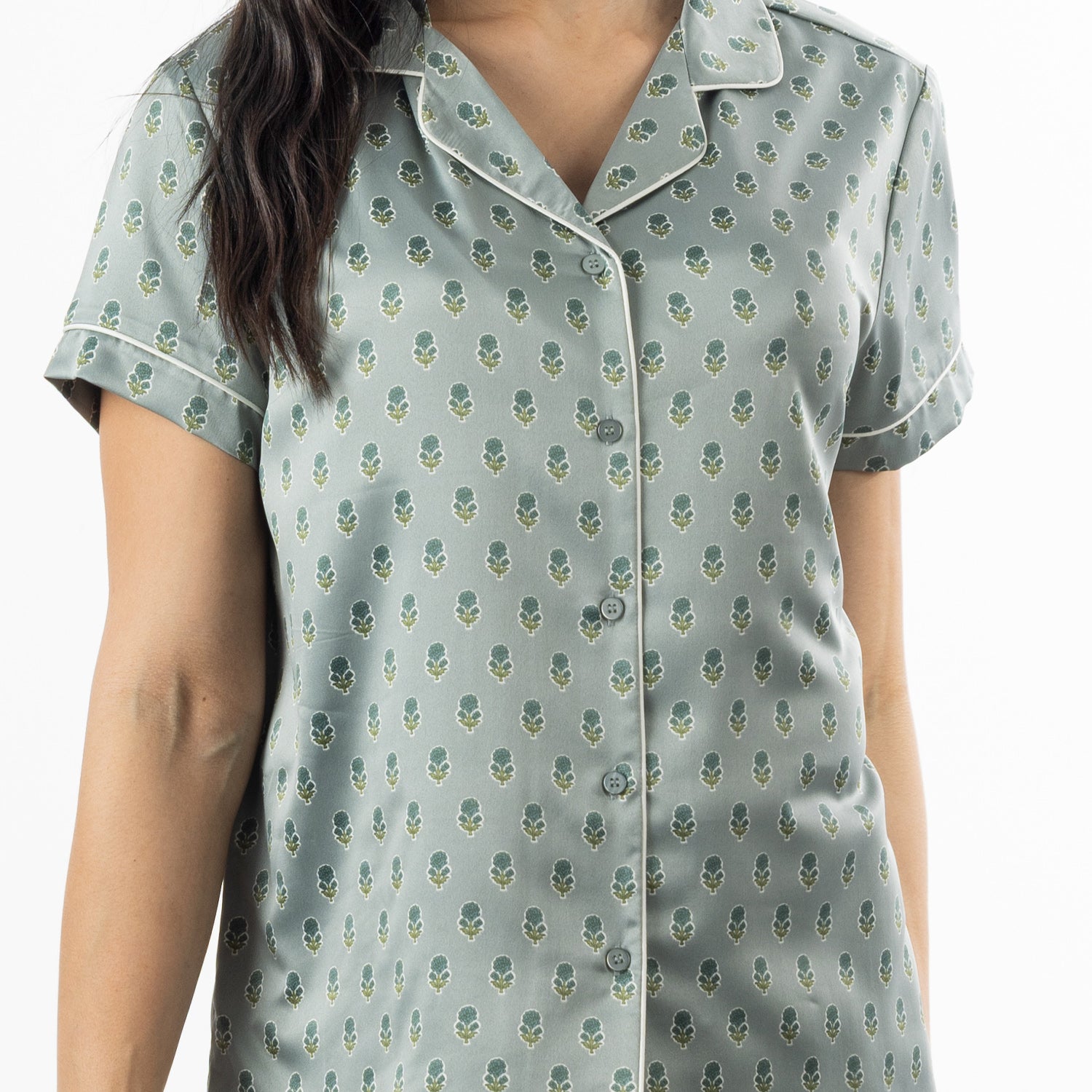 Close-up of the sage pyjama top, highlighting the button front, revere collar, small floral motif and contrast piping.