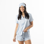 Woman modelling the pale blue floral satin pyjama set with a matching sleep mask.
