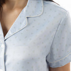 Close-up of the pale blue pyjama top, highlighting the delicate floral print, revere collar and contrast piping.