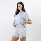A woman modeling a light blue graphic t-shirt and white pinstriped shorts with small yellow accents, standing against a plain white studio background.