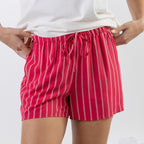 A person wearing bright red drawstring shorts with thin white vertical pinstripes, paired with a white top, shown from the waist to mid-thigh against a light gray studio background.
