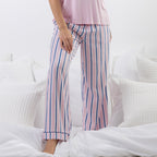 A person wearing pink pajama pants with vertical navy blue stripes, standing on a bed with white bedding and pillows.