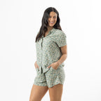Woman modelling the sage floral print short pyjama set from a slight side angle with hands in the shorts pockets.