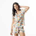 Woman modelling a multi-coloured summer fruit print pyjama set with a short sleeve button-up shirt and matching shorts.