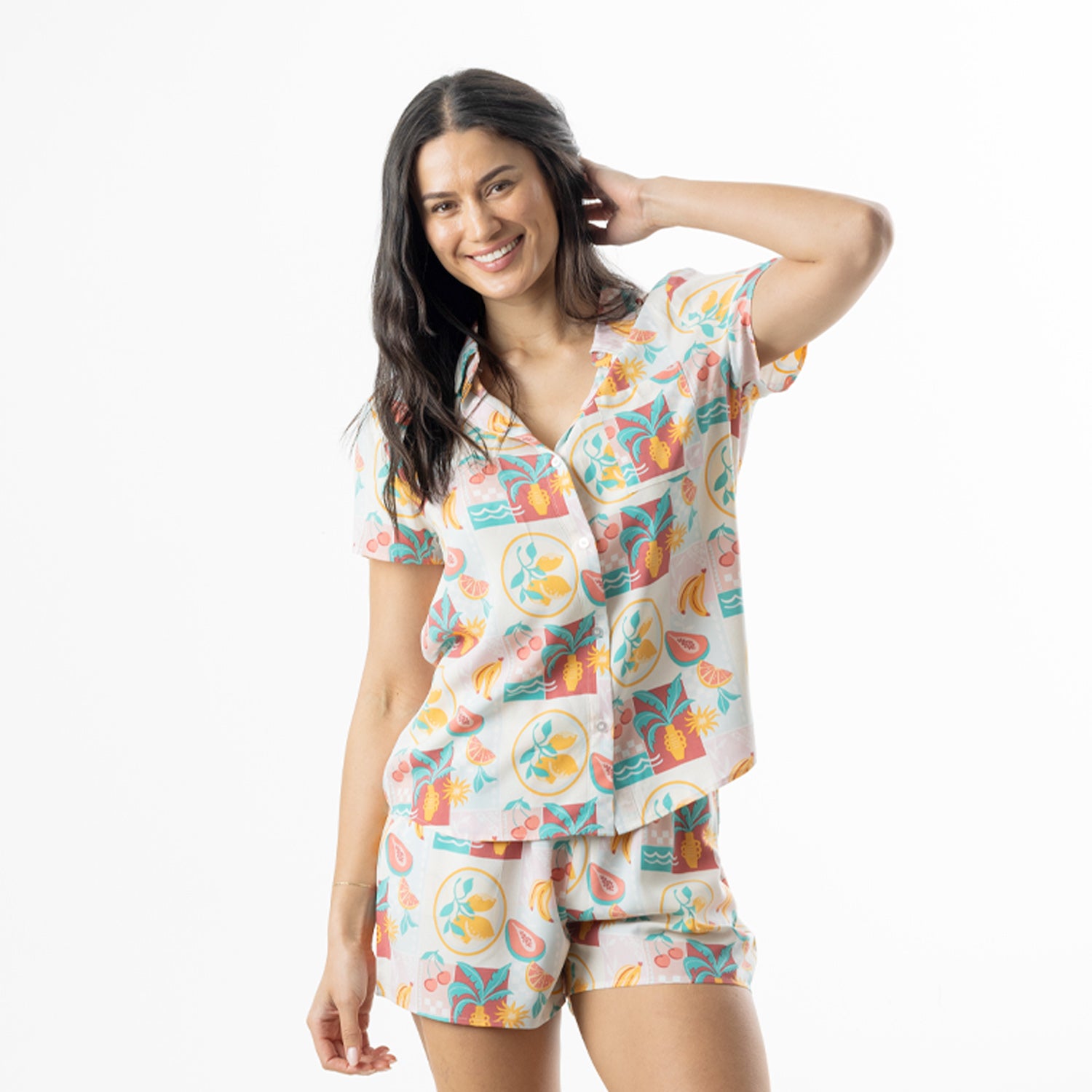 Woman modelling a multi-coloured summer fruit print pyjama set with a short sleeve button-up shirt and matching shorts.