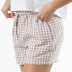 A close-up of a person wearing loose, gingham shorts in a natural and white check pattern with a matching drawstring waist. 