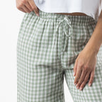 A close-up of a person wearing sage green and white gingham drawstring pants with a white cropped top, shown against a plain white background.