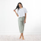 A woman stands barefoot in a bright room wearing a white short-sleeve crop top and sage-and-white gingham capri pants.