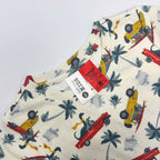Close-up of a children's cream-colored t-shirt featuring a colorful print of red and yellow cars, palm trees, and Dinos. close up of Tags.