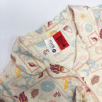 Close-up of a pajama top with a cream-colored base and a colorful mermaid and sea-themed print, featuring a visible brand label.