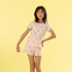 A young girl modeling a two-piece pajama set featuring a light pink base with a yellow and orange ice cream cone pattern, set against a solid pale yellow background.